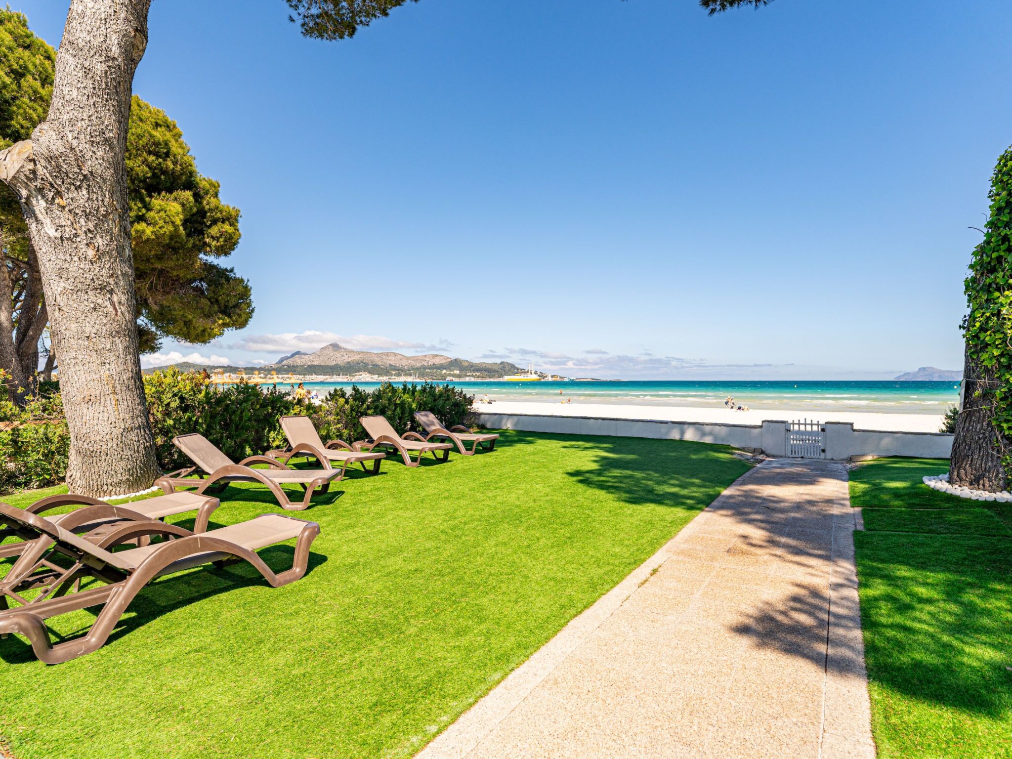 A pathway leading to beachside lounge chairs with a clear view of the sea and distant mountains.