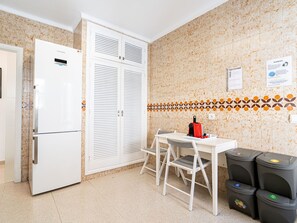 Eine kompakte Küche mit Kühlschrank, einem Doppeltürenschrank, einem kleinen Tisch mit Stühlen und zwei Mülleimern.