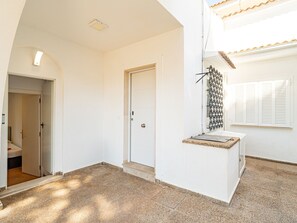 Ein Zimmer mit weißer Tür, einem kleinen Fenster mit Rollläden und einer Deckenleuchte.