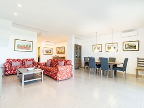 Ein geräumiger Wohnbereich mit einem roten, floralen Sofa, einem Esstisch mit Stühlen und Bildern an den Wänden.