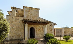 A stone building with a tiled roof, a central entrance with a staircase, and a small garden area with plants. - Villa Alejandra en Alcúdia by Interhome (Alcúdia)