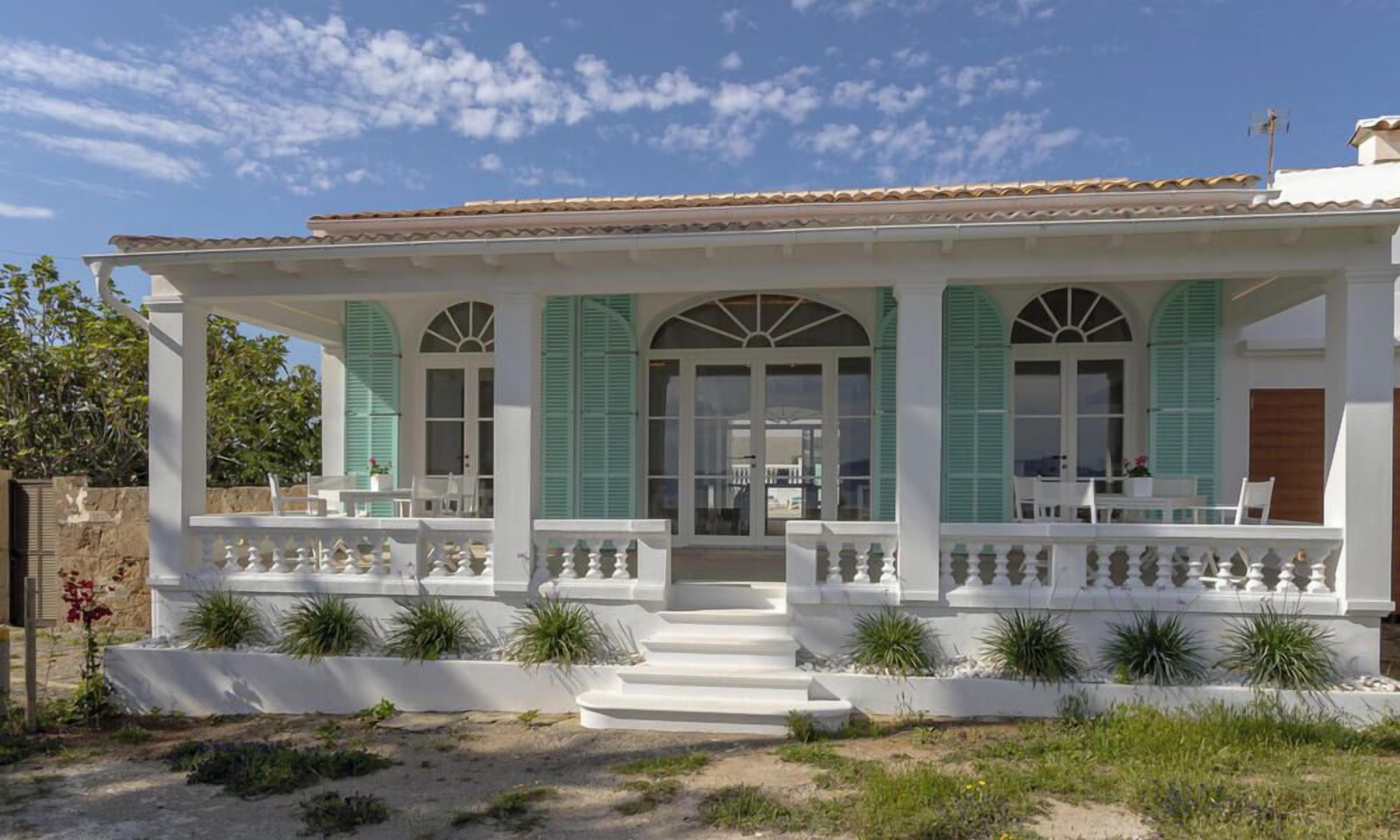 A white building with green shutters, a covered porch, and a tiled roof.