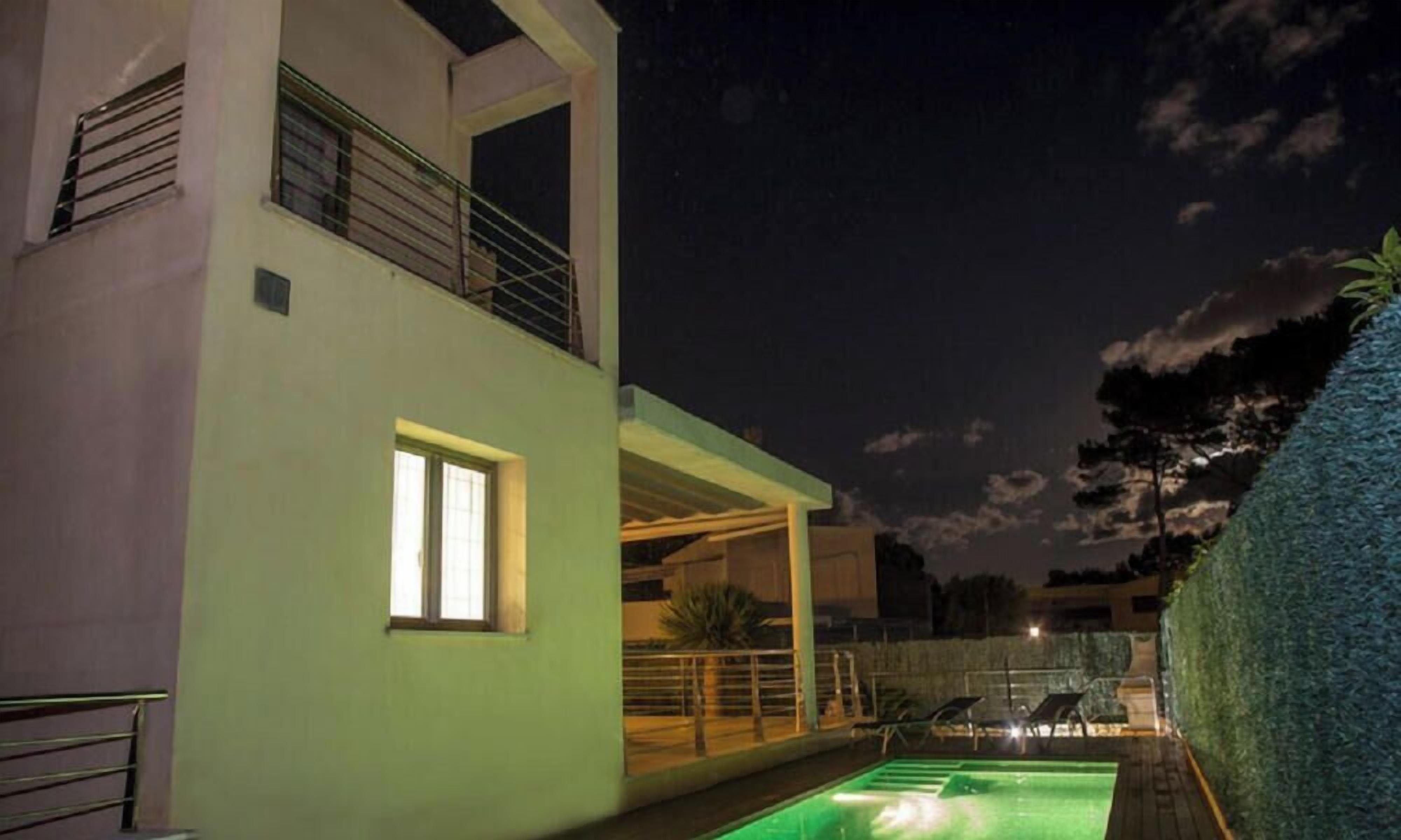 A modern building with a balcony, a pool, and a well-lit exterior.