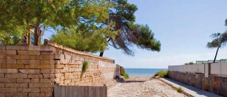 Une plage bordée d’un mur de pierres et d’une clôture en bois, qui mène à la mer.