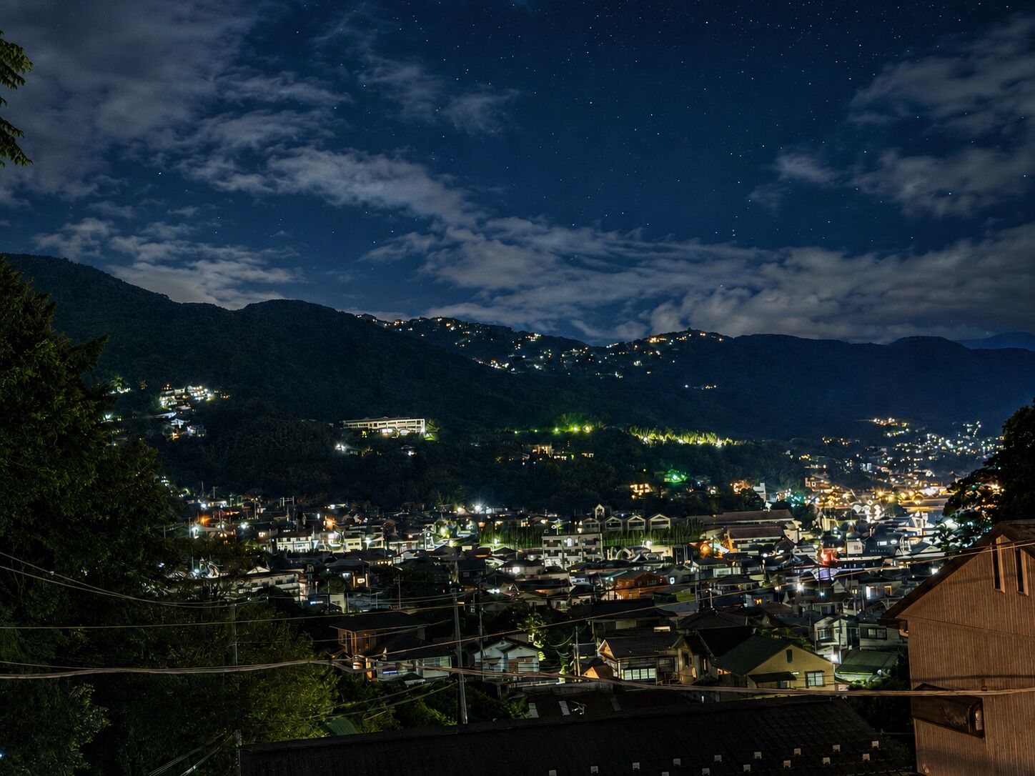 A nighttime view of a town with buildings and lights against a backdrop of mountains.