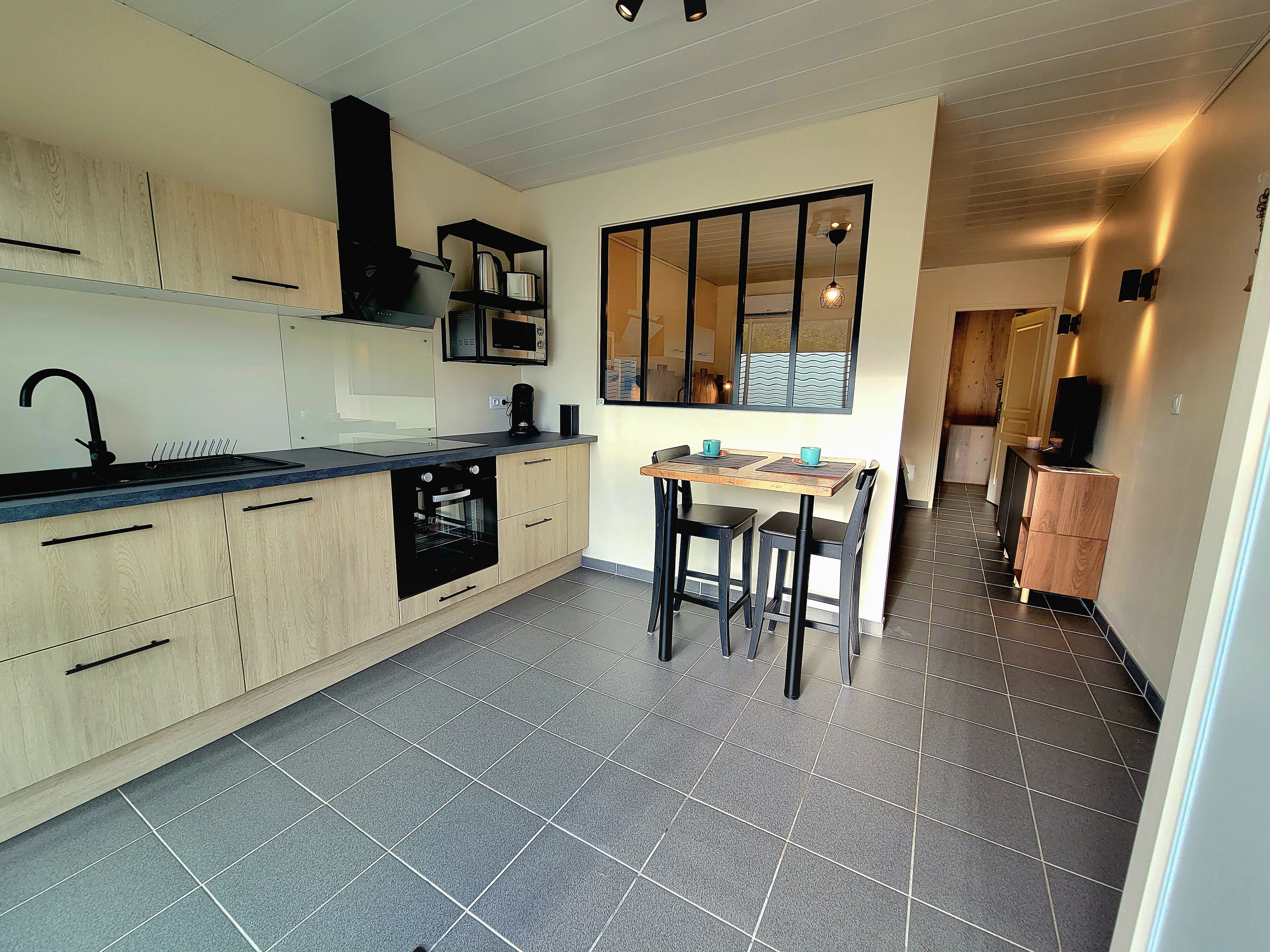 A modern kitchen with a built-in oven, a microwave, and a coffee maker. There is a dining area with a table and chairs.