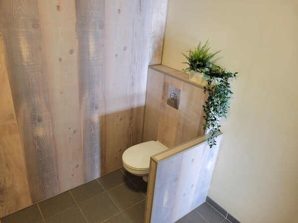 A wooden bathroom with a toilet, a small plant on the wall, and a tiled floor.