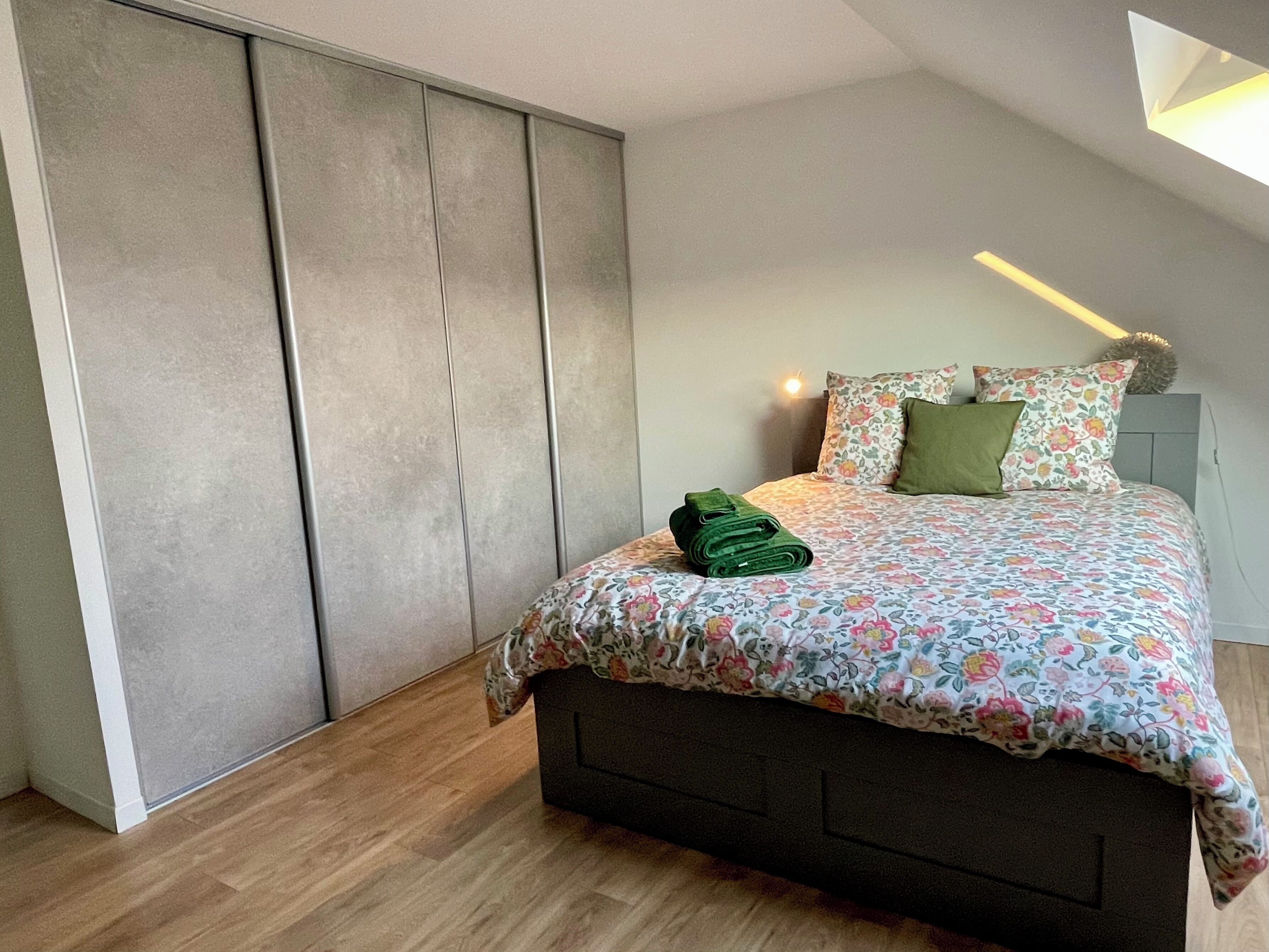 A bedroom with a bed, a nightstand, a lamp, and a wardrobe.