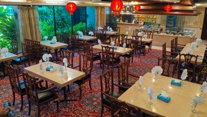 A restaurant with multiple tables and chairs, red lanterns, and a view of greenery outside.