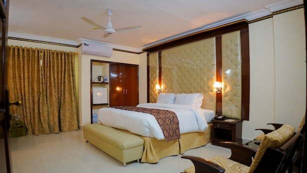 A hotel room with a bed, bedside table, chair, and an air conditioning unit.
