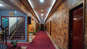 A hotel hallway with a red carpet, a staircase with blue patterned tiles, and stone walls.