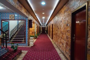 A hotel hallway with a red carpet, a staircase with blue patterned tiles, and stone walls.