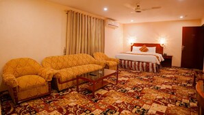 A hotel room with a sofa set, a bed with a headboard, a bedside table, and a patterned floor.