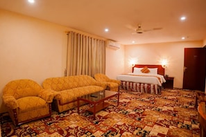 A hotel room with a sofa set, a bed with a headboard, a bedside table, and a patterned floor.