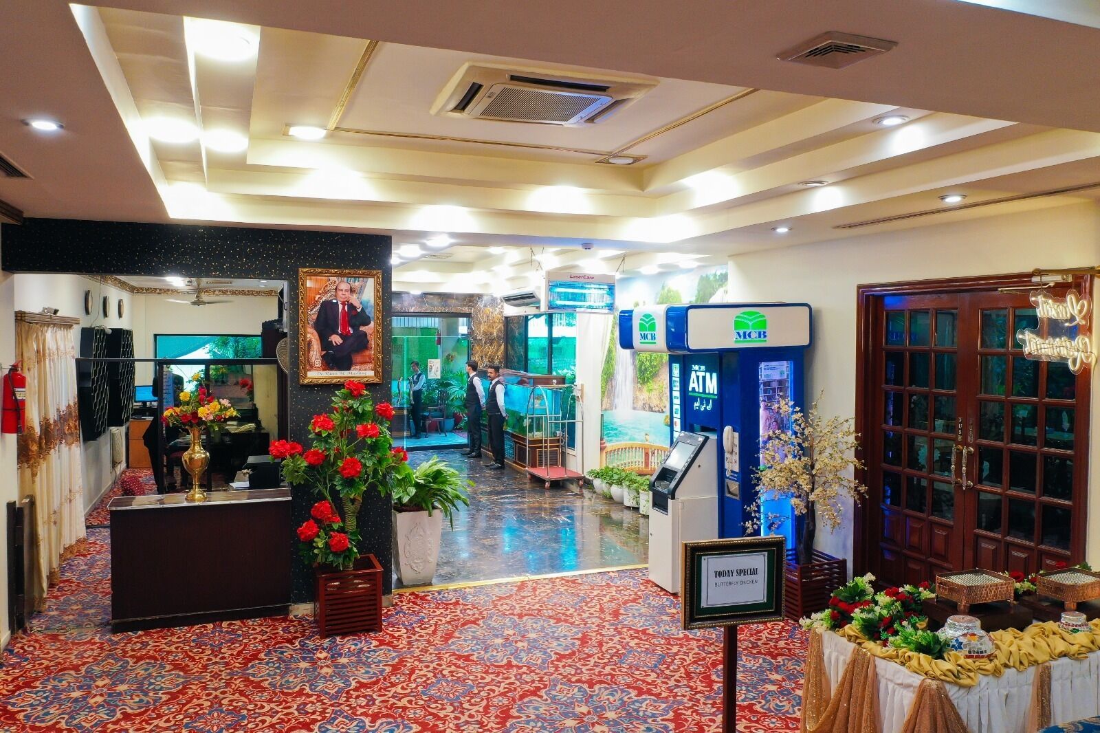Un vestíbulo de hotel con una recepción, un retrato enmarco y una planta decorativa.