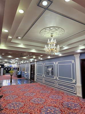 A spacious hotel lobby with a patterned carpet, ornate wall decorations, and a chandelier.
