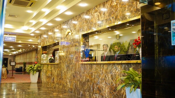 A hotel reception area with marble walls, a reception desk, and a clock.