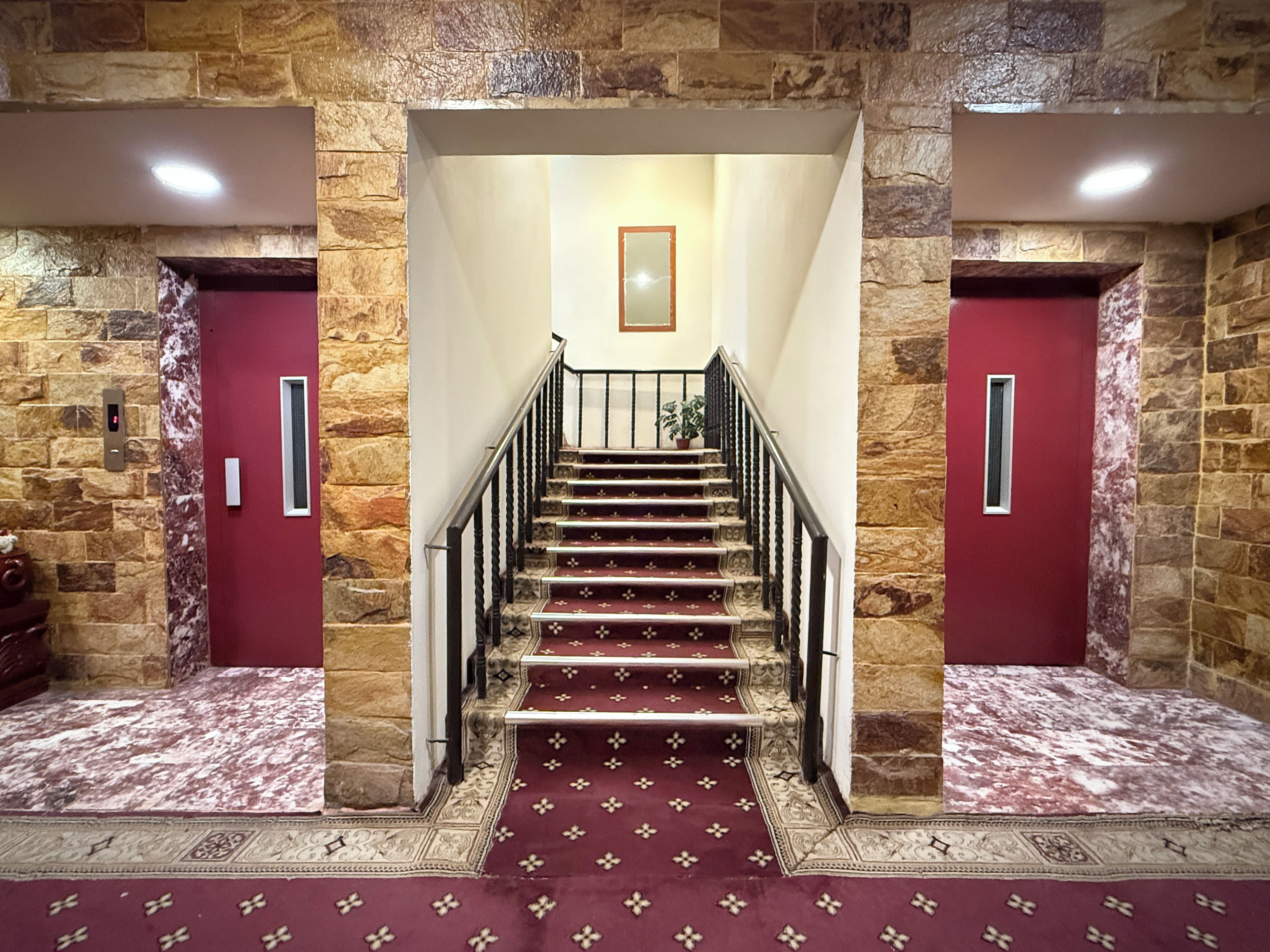 A staircase with a red carpet leading to a landing with a framed picture.