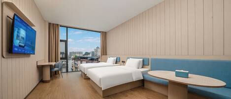 A hotel room with a bed, a sofa, a small table, and a TV on the wall.