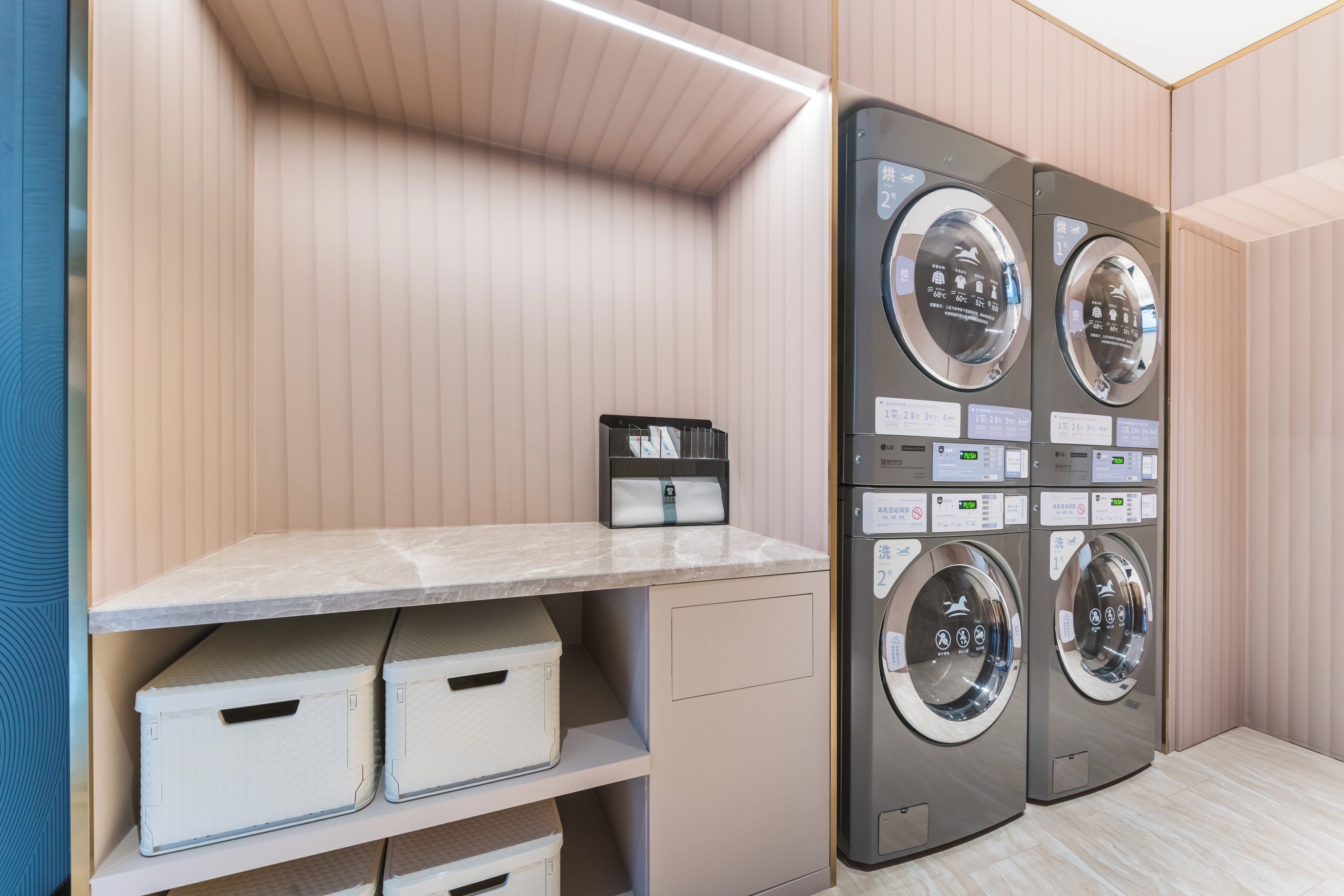 Une buanderie équipée de quatre machines à laver, d’une étagère où sont pliés les vêtements et de plusieurs bacs de rangement.