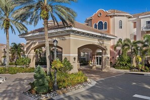 A hotel entrance with a covered patio, palm trees, and a clear blue sky. - Spacious 1-Bedroom Villa | Balcony (Orlando)