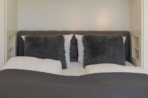 A bed with a grey headboard, two fluffy grey pillows, and white bedding. - Kyra - Westerland (Westerland)