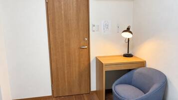 A small room with a wooden door, a desk with a lamp, and a blue chair.