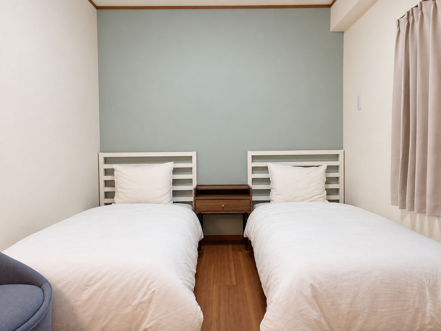 A twin room with two single beds, a wooden nightstand, and a light-colored wall.