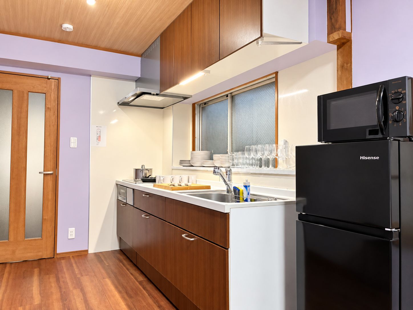 A compact kitchen with wooden cabinets, a stainless steel sink, and a black refrigerator.