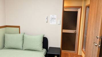 A bedroom with a bed, a nightstand, a door, and a wall-mounted light switch.