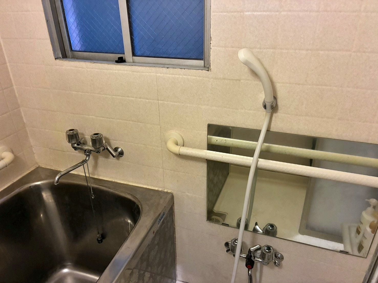 A bathroom with a stainless steel sink, a mirror, and a window with blue-tinted glass.