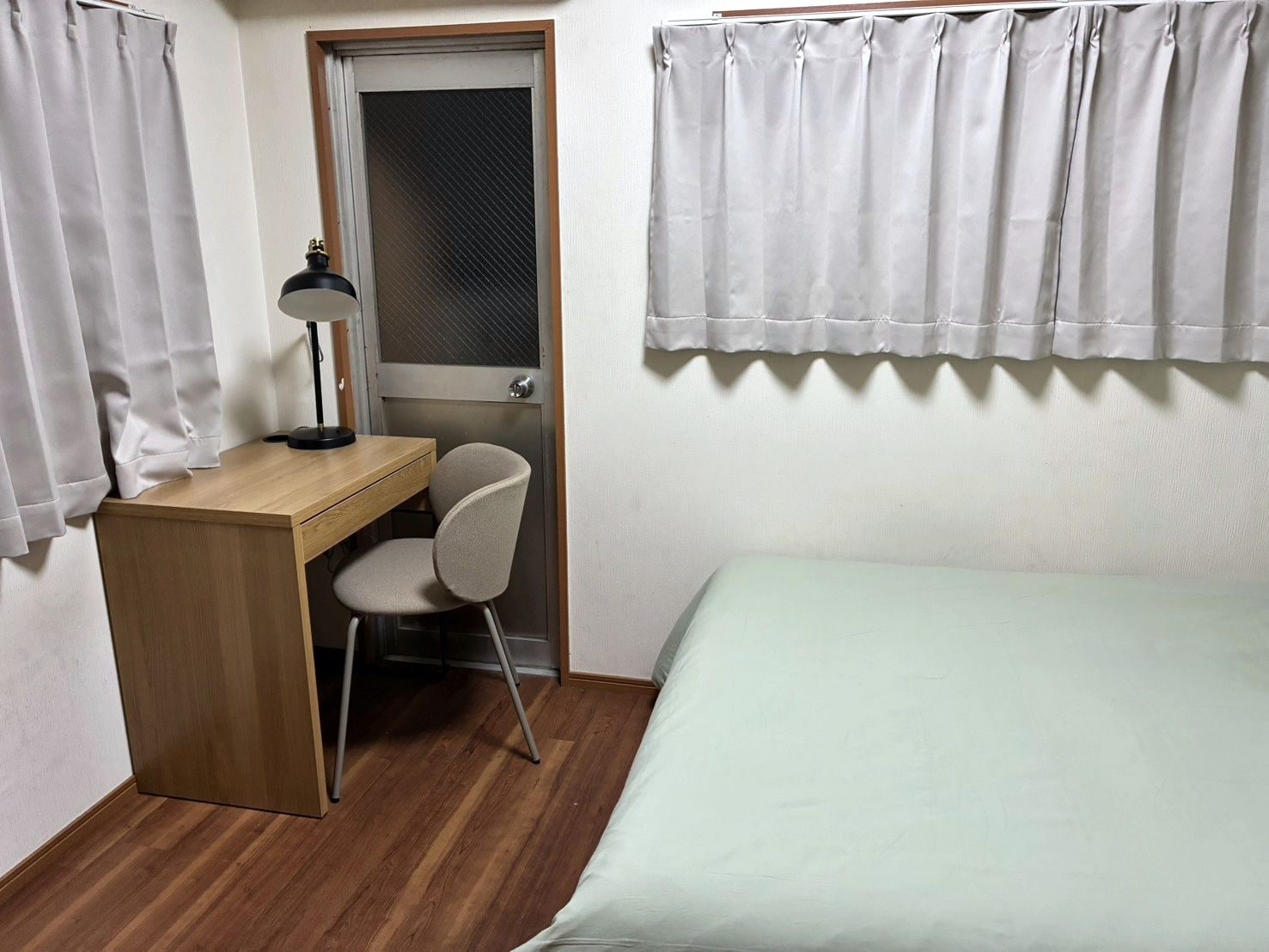 Una habitación pequeña con un escritorio de madera, una silla, una cama y una puerta con ventana.