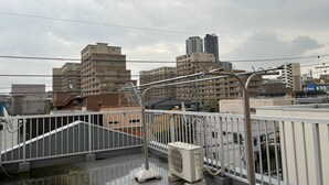 A rooftop terrace with a view of surrounding buildings, a metal railing, and an air conditioning unit. - The House Nagoya 5DK (Nakata, Chikusa-ku, Nagoya-shi)