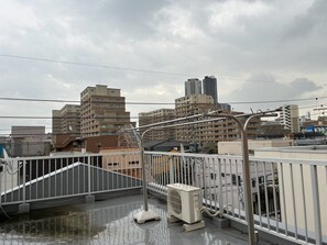 A rooftop terrace with a view of surrounding buildings, a metal railing, and an air conditioning unit. - The House Nagoya 5DK (Nakata, Chikusa-ku, Nagoya-shi)