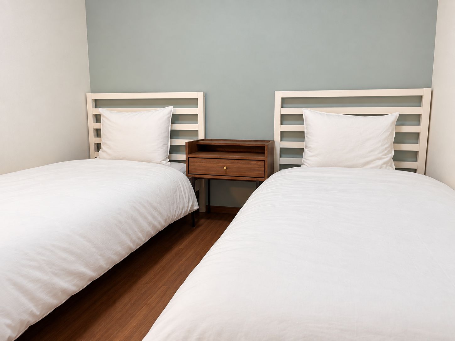 A twin room with two beds, a nightstand, and a wooden floor.