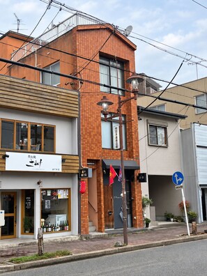 Un edificio de varios pisos con fachada de ladrillo, una tienda con un letrero y una señal de tráfico que indica una calle de un solo sentido.