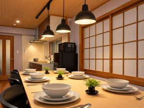 A traditional Japanese-style dining room with a low table set for four, black pendant lights, and a sliding shoji screen.