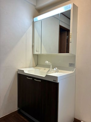 A bathroom with a white sink, a mirror, and dark wooden cabinets. - The House Nagoya 5DK (Nakata, Chikusa-ku, Nagoya-shi)