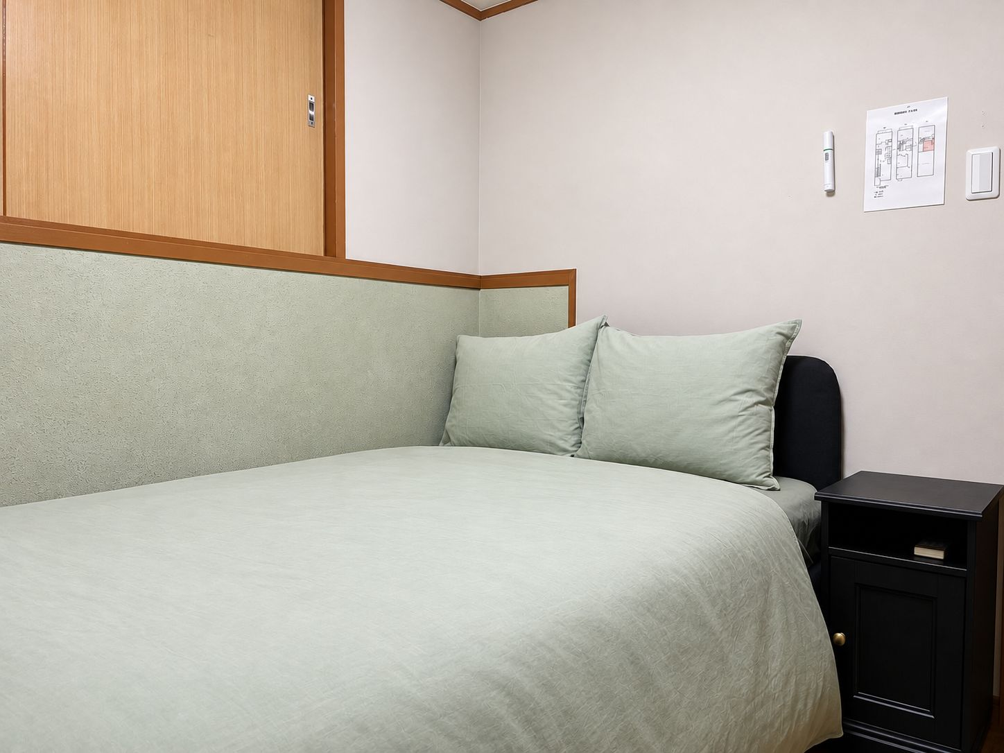 Una cama individual con cabecera, mesita de noche y un interruptor de luz en la pared.