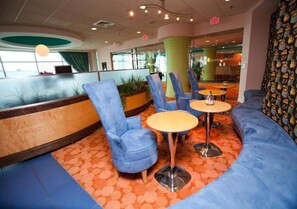 A seating area with blue chairs and round tables, a wooden bench, and a patterned orange carpet. - Ocean View 2BR Condo Steps from Beach (North Myrtle Beach)