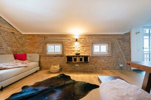 A cozy attic room with exposed brick walls, a wooden bench, a sofa, and a fur rug. - Watzmann Vacation Rental, 74 square meters (Schönau am Königssee)