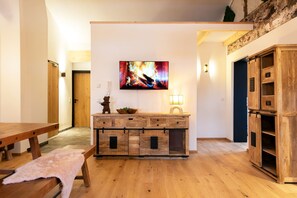 A living room with a wooden cabinet, a television mounted on the wall, and a bench. - Watzmann Vacation Rental, 74 square meters (Schönau am Königssee)