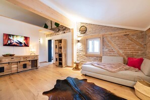 A cozy living room with a stone wall, a flat-screen TV, a wooden cabinet, a sofa, and a leather rug. - Watzmann Vacation Rental, 74 square meters (Schönau am Königssee)