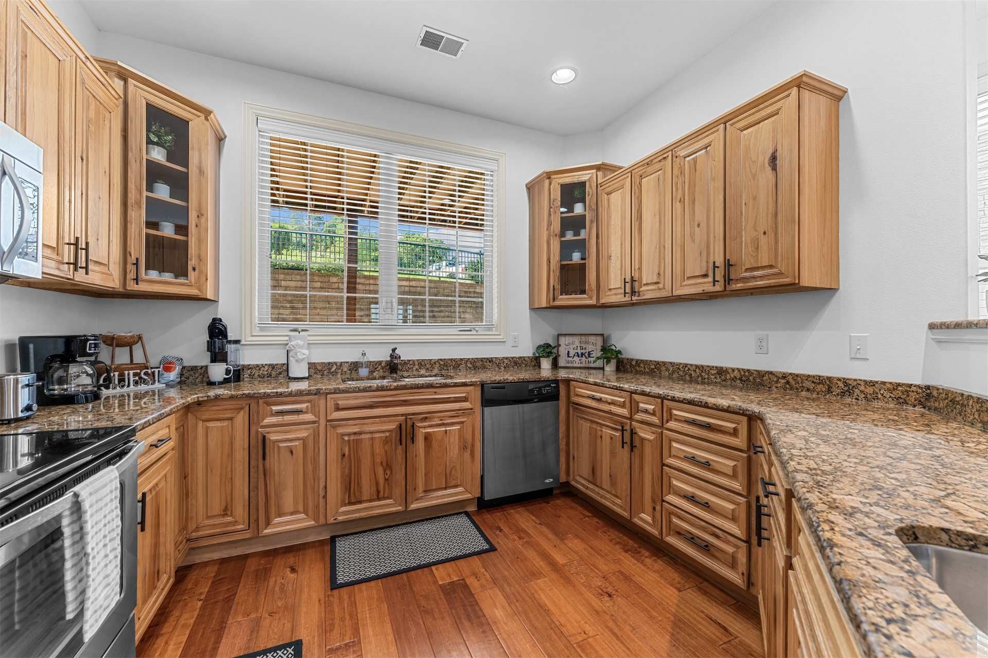 A kitchen with wooden cabinets, granite countertops, a dishwasher, and a window with blinds.