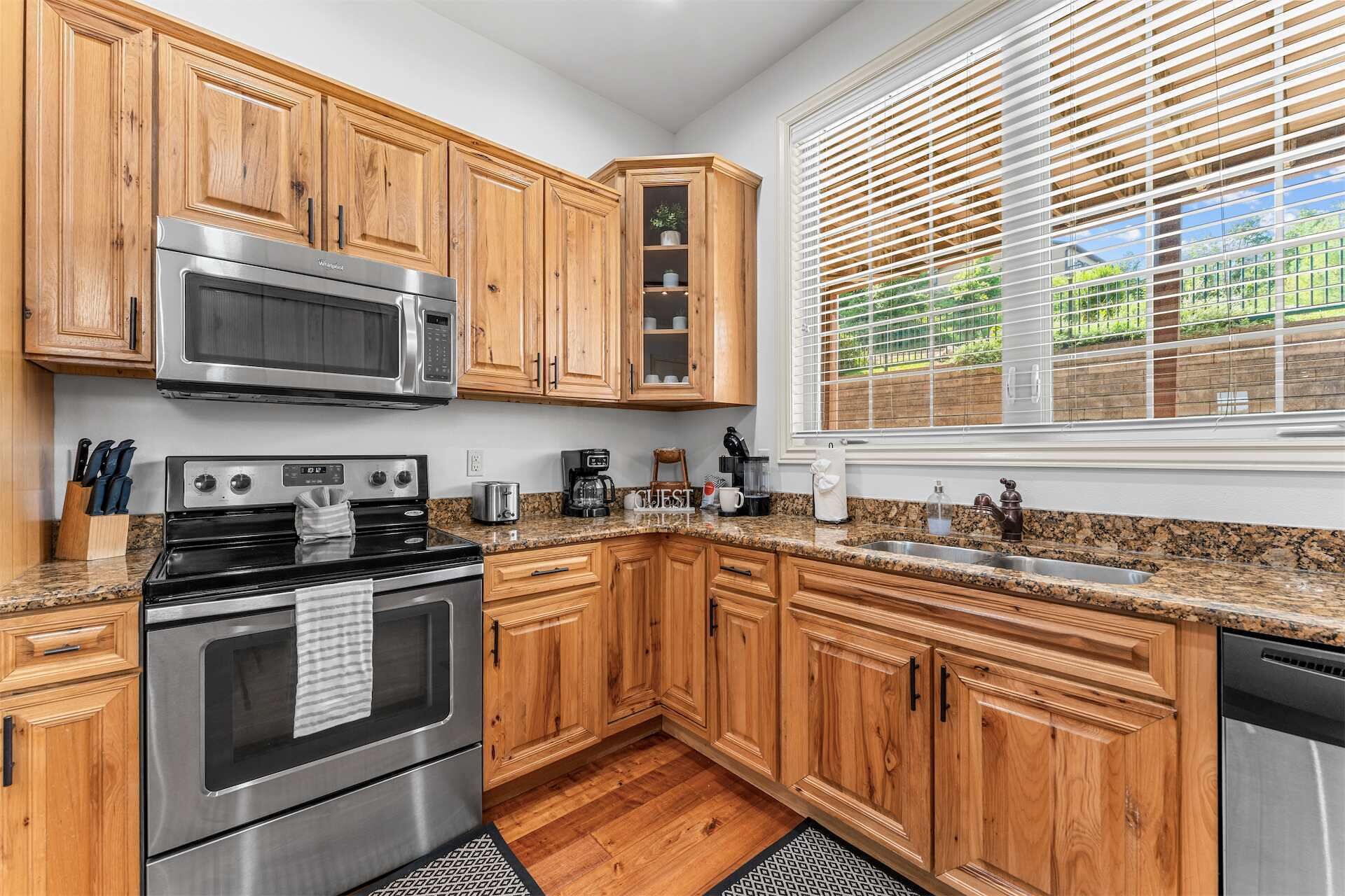 A kitchen with wooden cabinets, stainless steel appliances, a granite countertop, and a window with blinds.