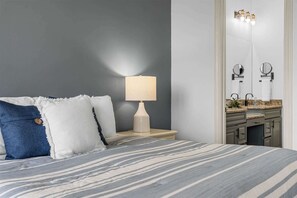 A bedroom with a bed, a bedside lamp, a nightstand, a mirror, and a bathroom with a sink and countertop. - Silver Dollar Awesome - 2bdr (Branson)