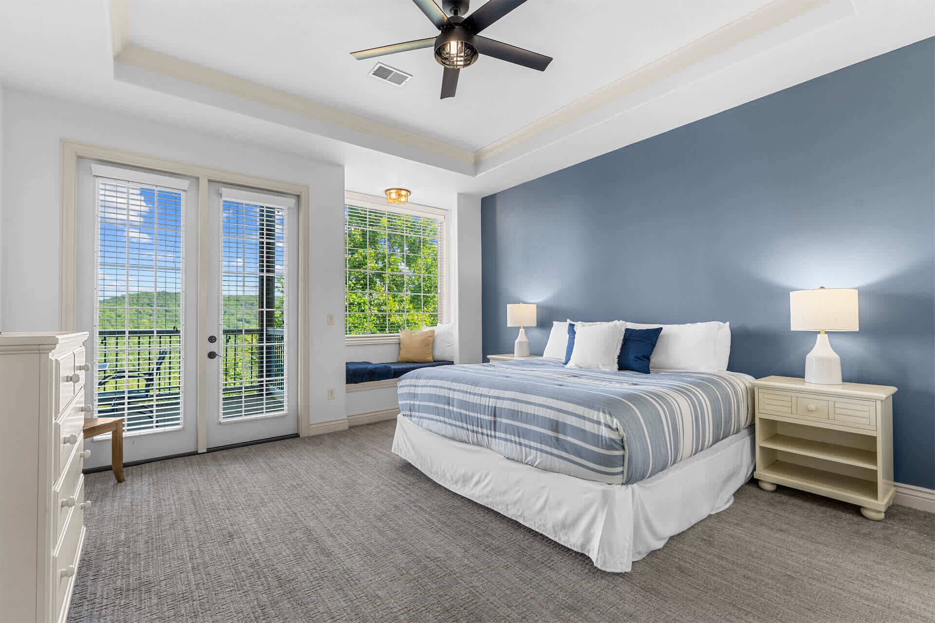 Une chambre à coucher avec un lit, des tables de chevet, un ventilateur de plafond et une vue par la fenêtre.