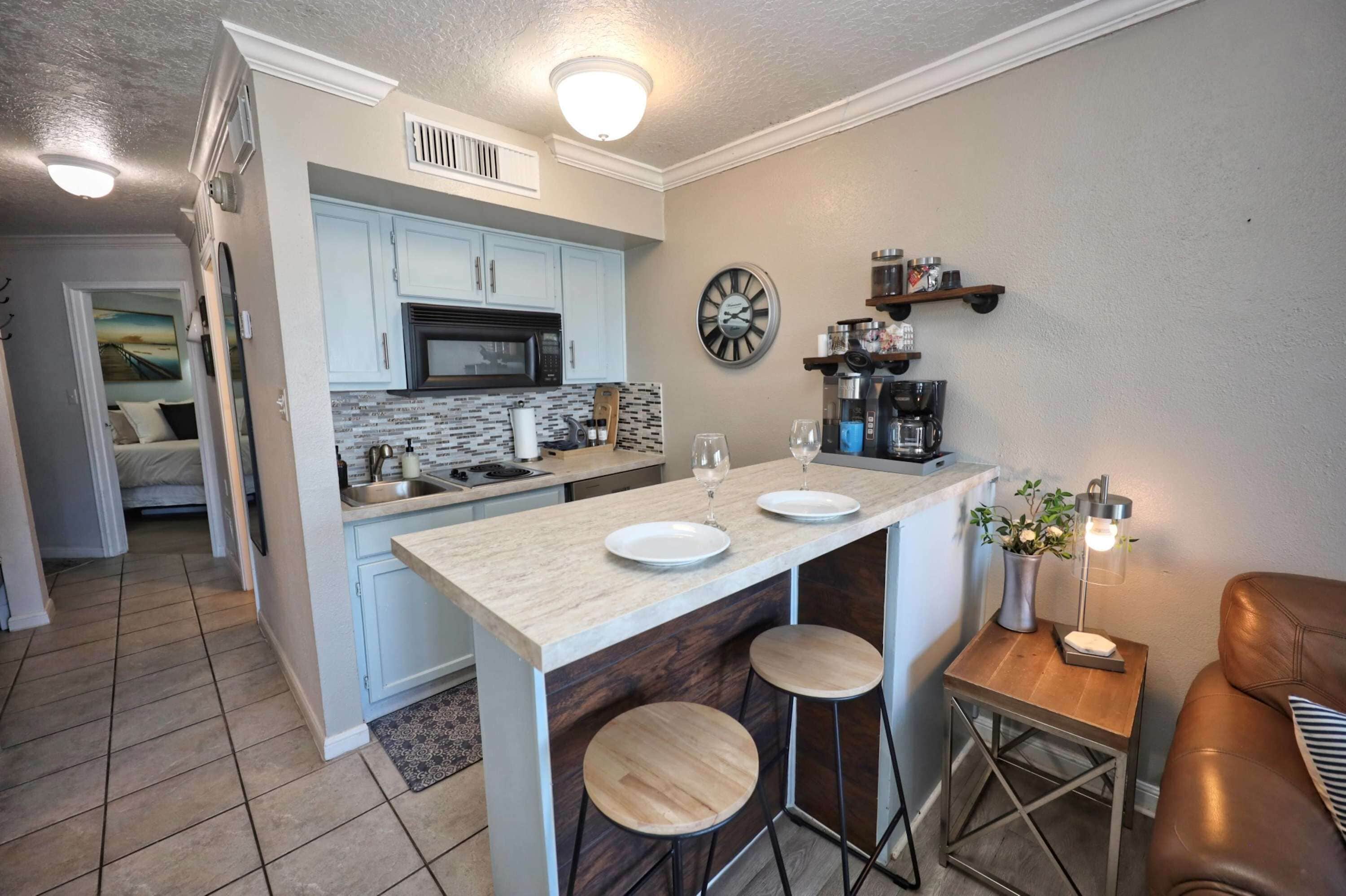 A modern kitchen with a central island, a dining area with stools, and a coffee station.