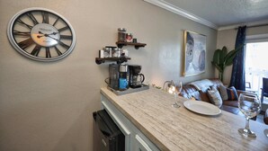 A kitchen with a large wall clock, coffee maker, and shelves with jars. - Seawall Serenity - Amenities (Galveston)
