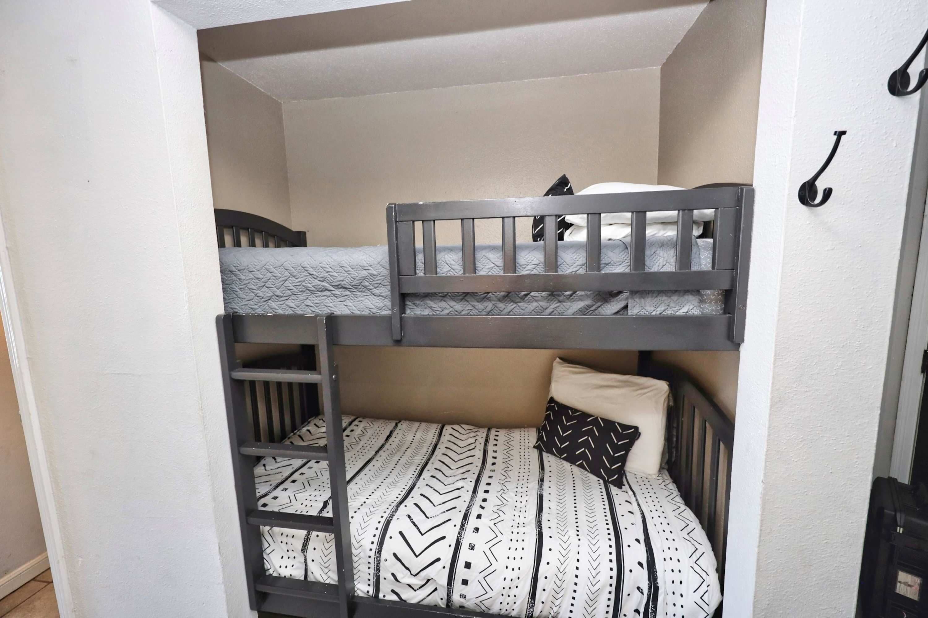 Una cama litera con escalera, una almohada y un gancho en la pared.